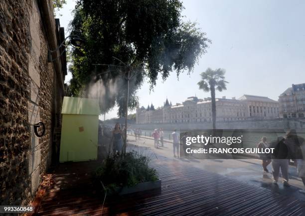 People walk past water sprays on the banks of the river Seine near la Conciergerie in Paris on July 7, 2018 during the 17th edition of Paris Plage...