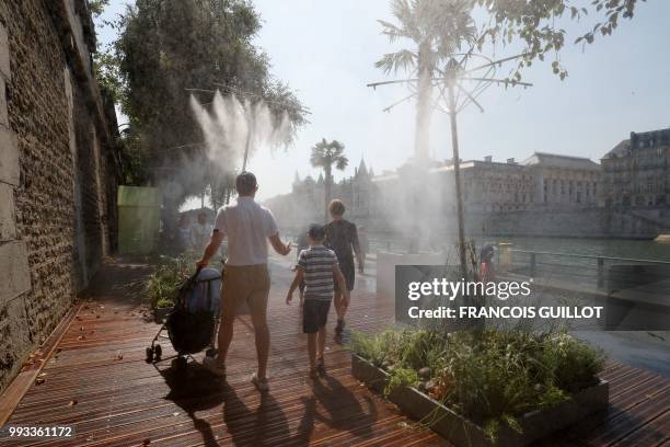 People walk past water sprays on the banks of the river Seine near la Conciergerie in Paris on July 7, 2018 during the 17th edition of Paris Plage...