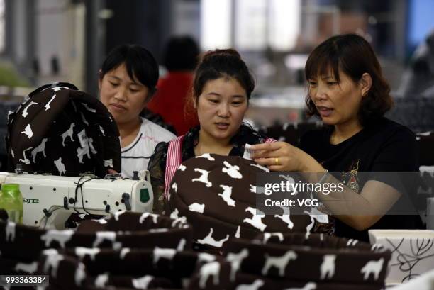 Chinese worker passes on her sewing skill of fabric doghouses to a new worker at a factory of Tancheng County on July 4, 2018 in Linyi, Shandong...