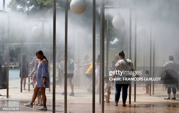 People walk under water sprays along the bassin de la Villette in Paris on July 7, 2018 during the 17th edition of Paris Plage summer event.