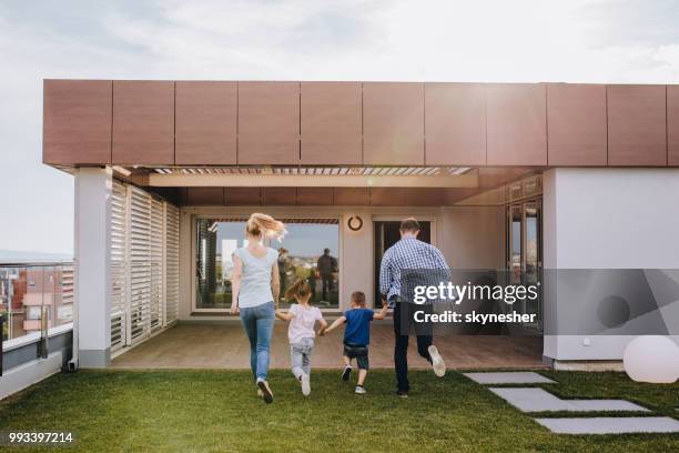 rear view of playful family having fun while holding hands and running on a penthouse balcony. - penthouse girl stock pictures, royalty-free photos & images