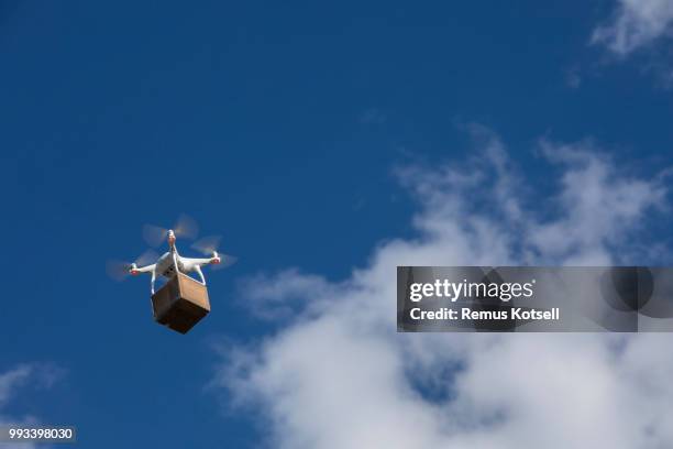 drone delivering a cardboard box on a blue sky. - drone parcel stock pictures, royalty-free photos & images