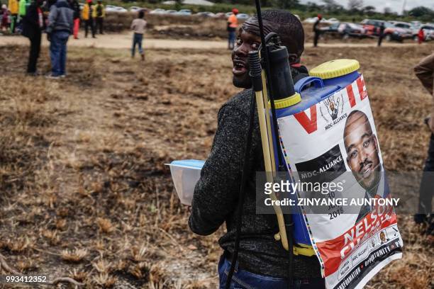 Man carries a fumigator with a campaign poster with the face of Movement for Democratic Change Alliance leader Nelson Chamisa at an election rally on...