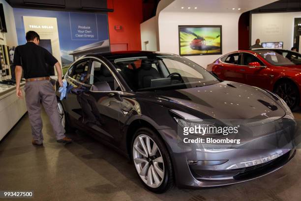 An employee cleans a Tesla Inc. Model 3 electric vehicle on display at the company's showroom in Newport Beach, California, U.S., on Friday, July 6,...