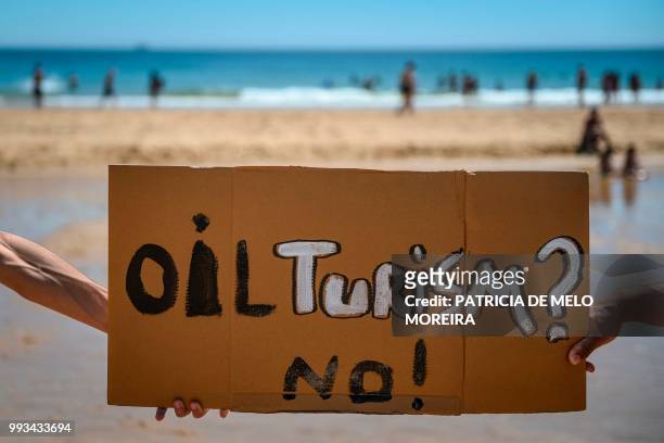 Dozens of protesters hold banners and gather to protest against the oil exploration off the southern coast at Carcavelos beach in Cascais, in the...