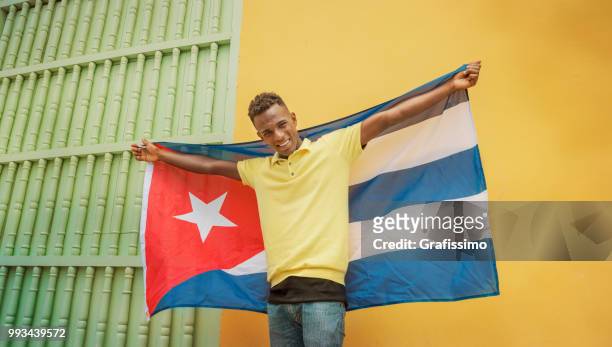 kubanische mann lächelnd, blick in die kamera in alt-havanna kuba mit kubanischen flagge - grafissimo stock-fotos und bilder