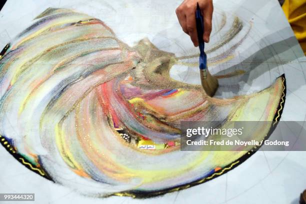 a tibetan monk uses a paint brush to blend colored sand mandal and sweep it into a pile. - blend stockfoto's en -beelden