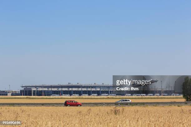 a passenger airplane takes off in berlin-schönefeld airport with new terminal building in the background (brandenburg, germany) - volkswagen to store thousands of cars at new berlin airport stockfoto's en -beelden