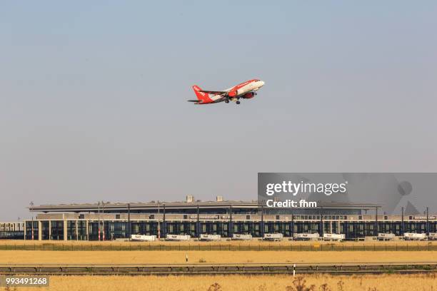 a passenger airplane takes off in berlin-schönefeld airport with new terminal building in the background (brandenburg, germany) - schoenefeld stock-fotos und bilder