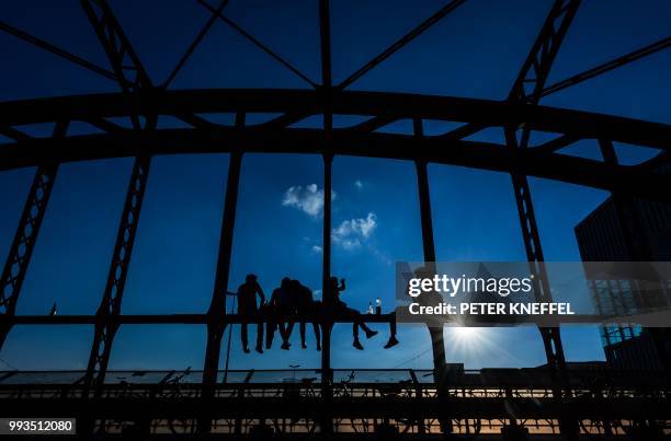 Young people sit on a bridge and have a drink as the sun goes down in Munich, southern Germany on July 7, 2018. / Germany OUT