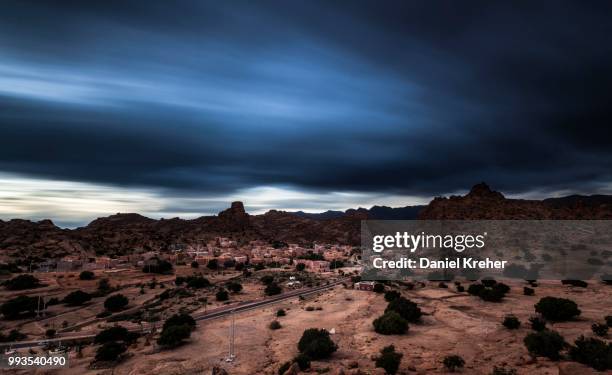 small village of aguard oudad with brightly painted houses in front of the rock chapeau napoleon, dramatic clouds, evening, tafraoute, anti atlas, southern morocco, morocco - chapeau stock pictures, royalty-free photos & images