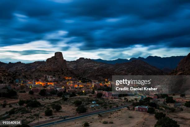 small village of aguard oudad with brightly painted houses in front of the rock chapeau napoleon, dramatic clouds, evening, tafraoute, anti atlas, southern morocco, morocco - chapeau ストックフォトと画像