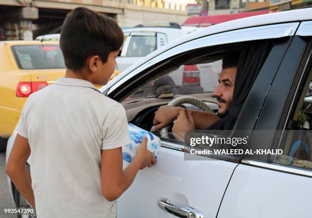 An Iraqi child peddlar sells tissue paper to cars driving down a street in the northern Iraqi city of Mosul on July 7, 2018. - A year on from Iraqi...