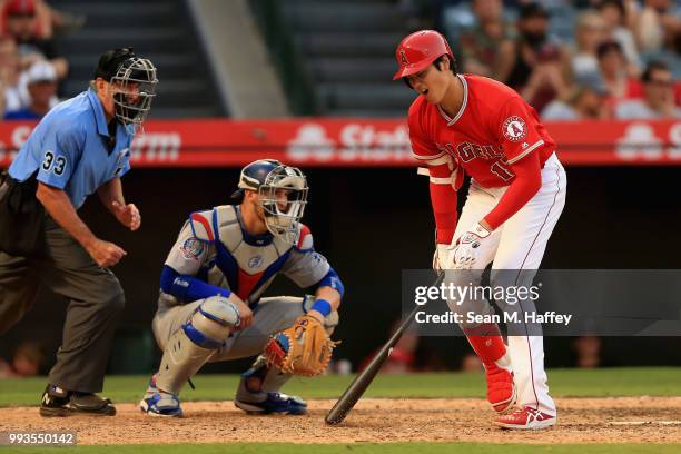 Shohei Ohtani of the Los Angeles Angels of Anaheim reacts to hitting a foul ball off of his knee as Yasmani Grandal of the Los Angeles Dodgers and...