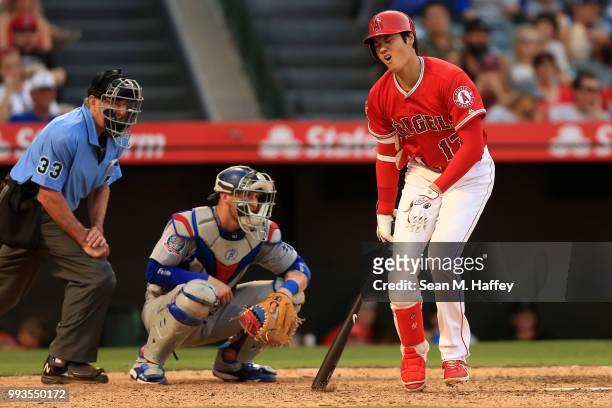 Shohei Ohtani of the Los Angeles Angels of Anaheim reacts to hitting a foul ball off of his knee as Yasmani Grandal of the Los Angeles Dodgers and...