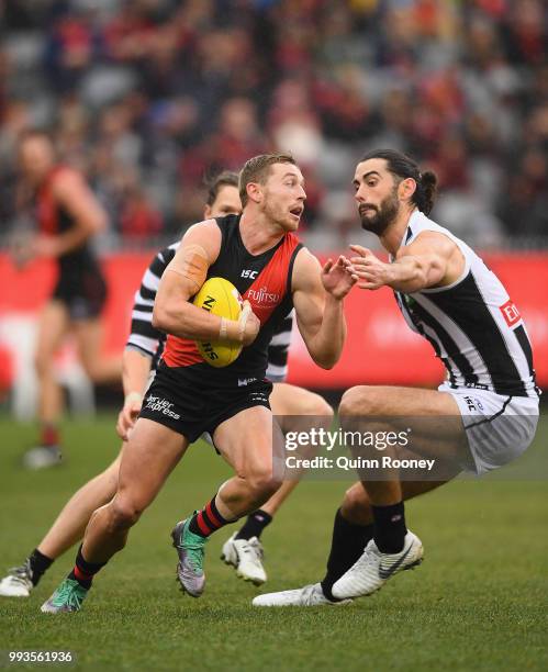 Devon Smith of the Bombers gets around a tackle by Brodie Grundy of the Magpies during the round 16 AFL match between the Essendon Bombers and the...