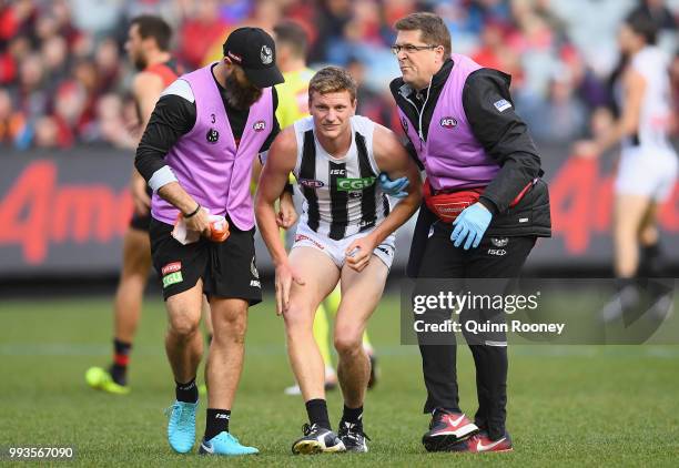 Will Hoskin-Elliott of the Magpies is attended to by trainers during the round 16 AFL match between the Essendon Bombers and the Collingwood Magpies...