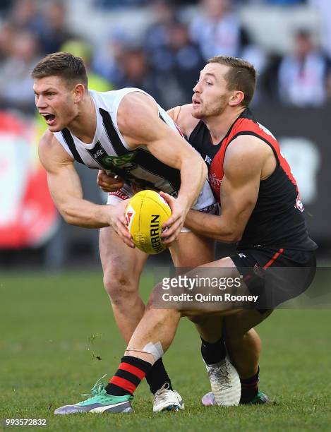 Taylor Adams of the Magpies is tackled by Devon Smith of the Bombers during the round 16 AFL match between the Essendon Bombers and the Collingwood...