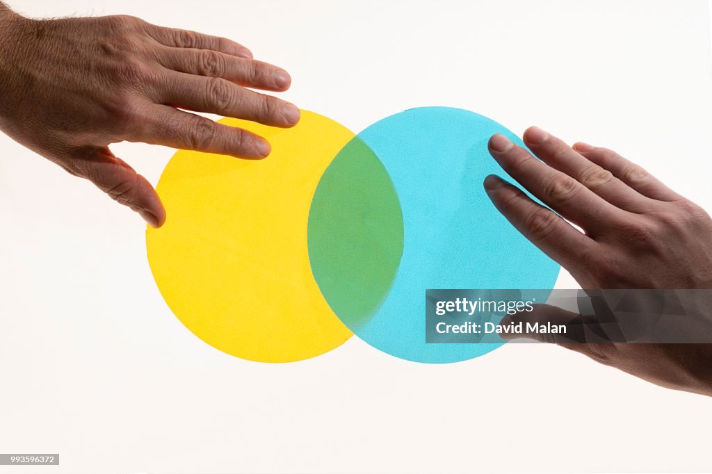 Two hands positioning translucent circles to form a venn diagram.