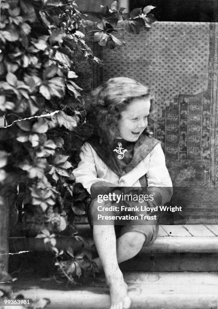 John Wright on the front steps of the home at approximately 4 years of age, rug hanging behind John off the front gate, lush foliage to the left, at...