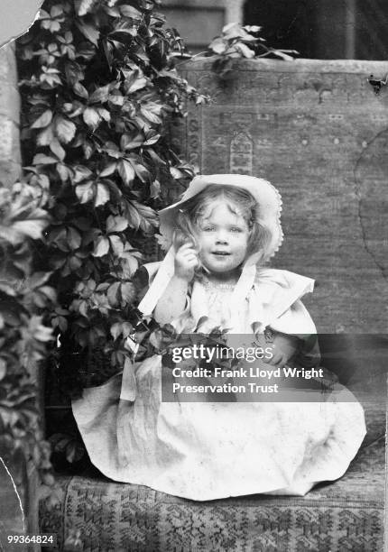 Catherine Wright on front porch of home at approximately 2 years of age, rug beneath and behind her obstructs the view of the home, lush foliageto...