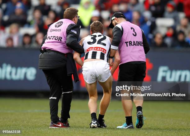 Will Hoskin-Elliott of the Magpies is helped from the field during the 2018 AFL round 16 match between the Essendon Bombers and the Collingwood...