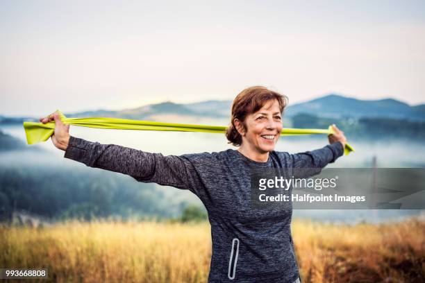 Senior woman exercising with resistance bands outdoors in nature in the foggy morning.