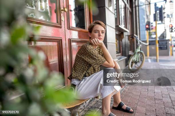 serious young woman sitting on skateboard at the door - waiting stock-fotos und bilder