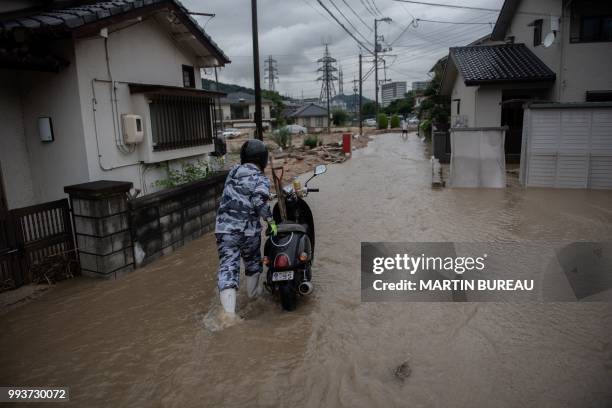 Man pushes his scooter through a flooded street in Saka, Hiroshima prefecture on July 8, 2018. - Japan's Prime Minister Shinzo Abe warned on July 8...