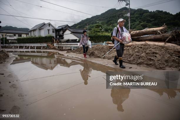Man and his wife carrying their belongings walk past a devastated street during floods in Saka, Hiroshima prefecture on July 8, 2018. - Japan's Prime...