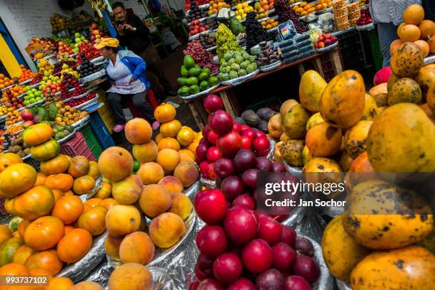 Colombian vendor sits on a box behind piles of fruit at Paloquemao market on November 25, 2017 in Bogota, Colombia.