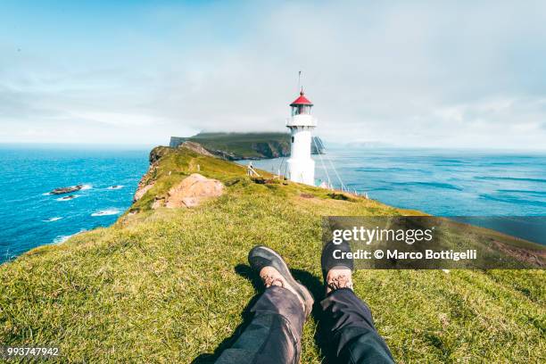 tourist relaxing at the mykines lighthouse - pov shoes stock-fotos und bilder