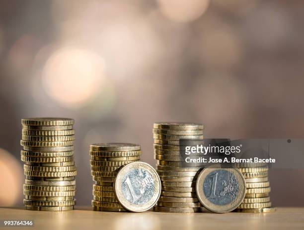 euro  coins arranged in heaps of different sizes, on a table illuminated by the light of the sun. - zwei euro münze stock-fotos und bilder