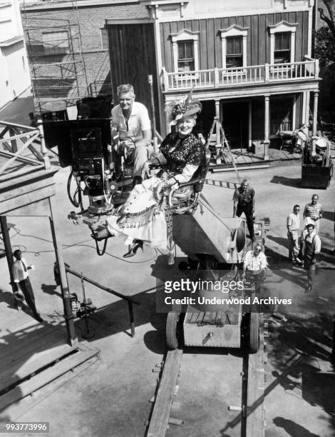 Portrait of American actress Shirley Booth , in full costume, and cinematographer Charles Lang as they sit on a camera boom above the backlot set of...