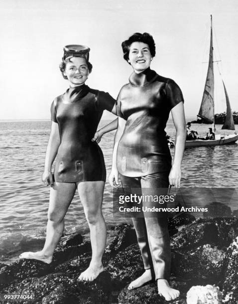 Heavily retouched photo features two unidentified women as they model neoprene wetsuits on a rocky beach, Berkeley, California, March 1954.