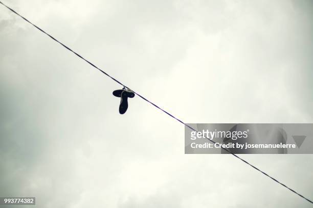 sneakers hanging from a cable in a city - josemanuelerre fotografías e imágenes de stock