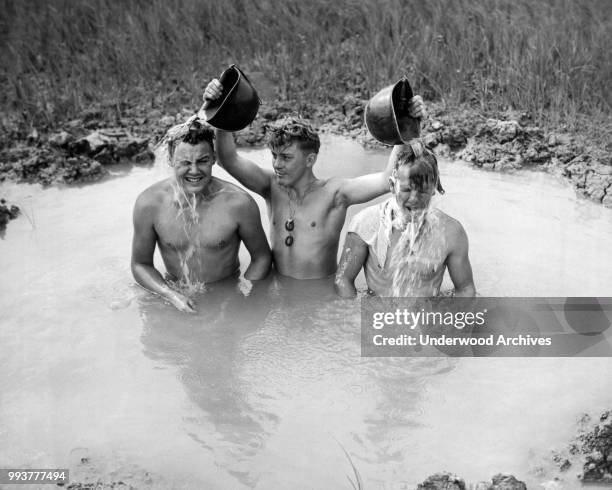 View of a trio of unidentified American soldiers, tankmen of the Sixth Marine Division, as they bath in a shell hole, Okinawa, Japan, June 1945.