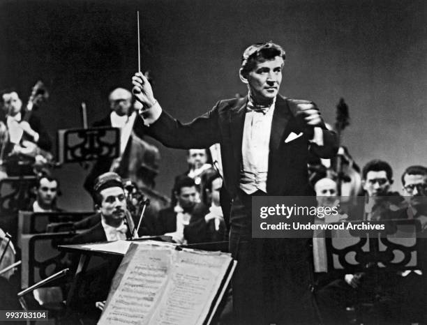 American composer, musician, and conductor Leonard Bernstein , of the New York Philharmonic, as he conducts and orchestra, New York, New York,...