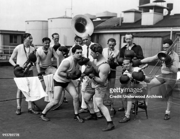 British-born lightweight boxer turned musician Sid Marks lands a 'punch' on another man as members of his orchestra, all in boxing gear, hold their...