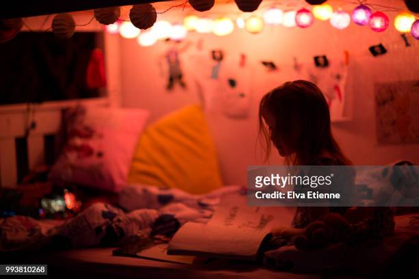 girl reading herself a book in bed at bedtime, under the warm glow of a string of night lights - bedtime stories stock-fotos und bilder