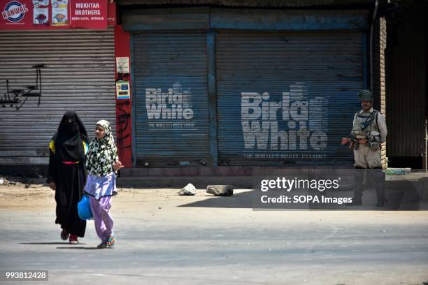 Kashmiri locals walk past an Indian policeman standing guard during restrictions imposed on the second death anniversary of the rebel commander...