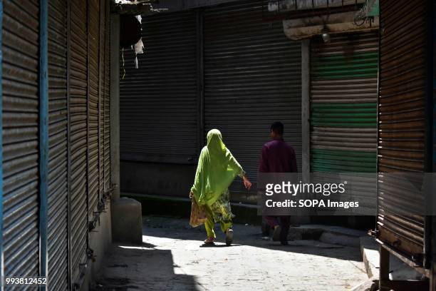 Kashmiri locals walk past closed shops during the curfew imposed on the eve of the second death anniversary of the rebel commander Burhan Muzaffar...