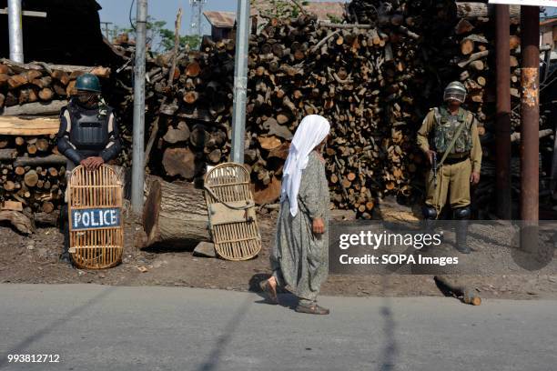 Indian government forces stands guard as a Kashmiri old woman walks in front on the deserted streets during a curfew restrictions, on the second...