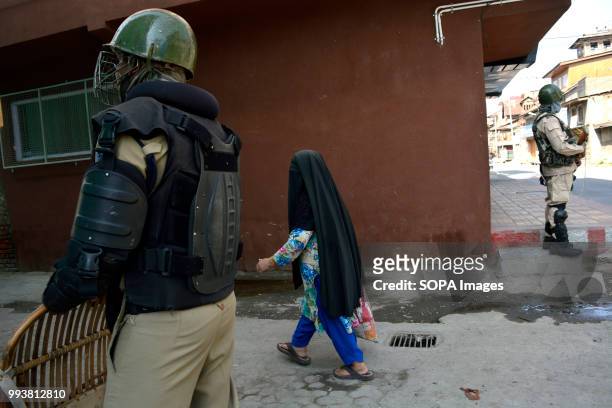 Indian government forces stands guard as a burqa clad Kashmiri woman walks past on the deserted streets during a curfew restrictions, on the second...