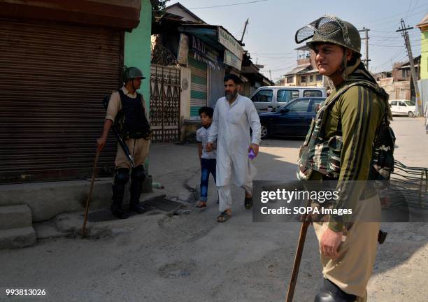 Indian paramilitary troops stands guard as a Kashmiri man along with his son walks in front during a curfew restrictions, on the second death...