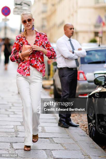 Guest wears a red floral print shirt, white flared pants, brown shoes, sunglasses, purple long earrings , during Paris Fashion Week Haute Couture...