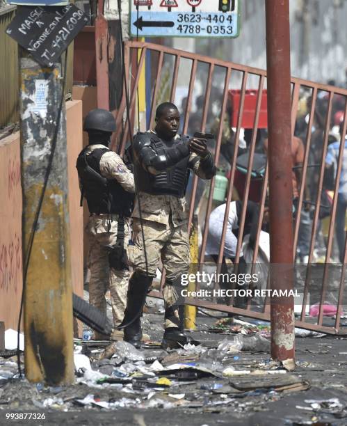 Member of the Haitian police points his gun at people to avoid looting in shops in Delmas, a commune near Port au Prince during protests against the...