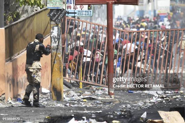 Member of the Haitian police points his gun at people to avoid looting in shops in Delmas, a commune near Port au Prince during protests against the...