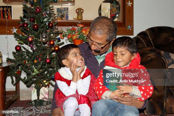 little sisters holding holy bible while sitting in their father lap on the eve of christmas 2017 - amir mukhtar stock pictures, royalty-free photos & images