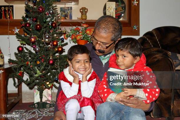 little sisters holding holy bible while sitting in their father lap on the eve of christmas 2017 - amir mukhtar stock pictures, royalty-free photos & images